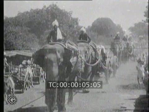 INDES. ATTELES A L'ARTILLERIE HINDOUE LES ELEPHANTS TIRENT DE LOURDES PIECES EN TERRAIN ACCIDENTE ET S'OFFRENT ENSUITE UN RAFRAICHISSEMENT BIEN MERITE (India. Harnessed to Hindu Artillery, Elephants Draw Heavy Parts on Rough Ground and are Rewarded a Refr